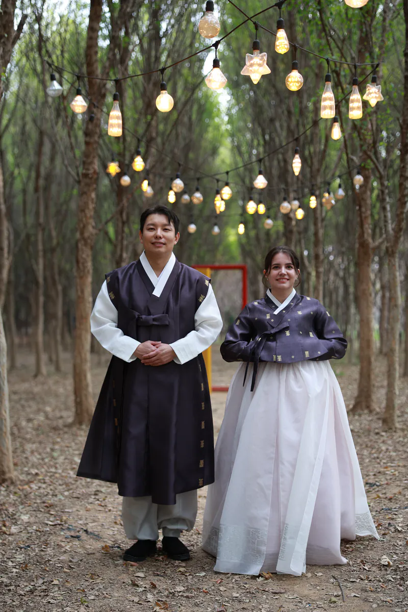 Sara e Jiwon con hanbok baixo luces colgadas nun bosque